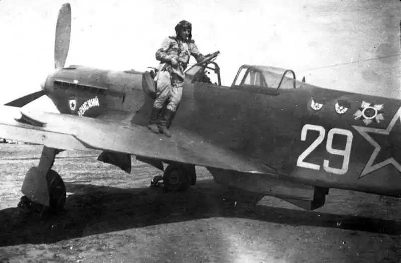 Soviet pilot N. F. Kizim in flight gear standing on the wing of a Yakovlev Yak-9U fighter at an airfield in Bulgaria, 1945.
