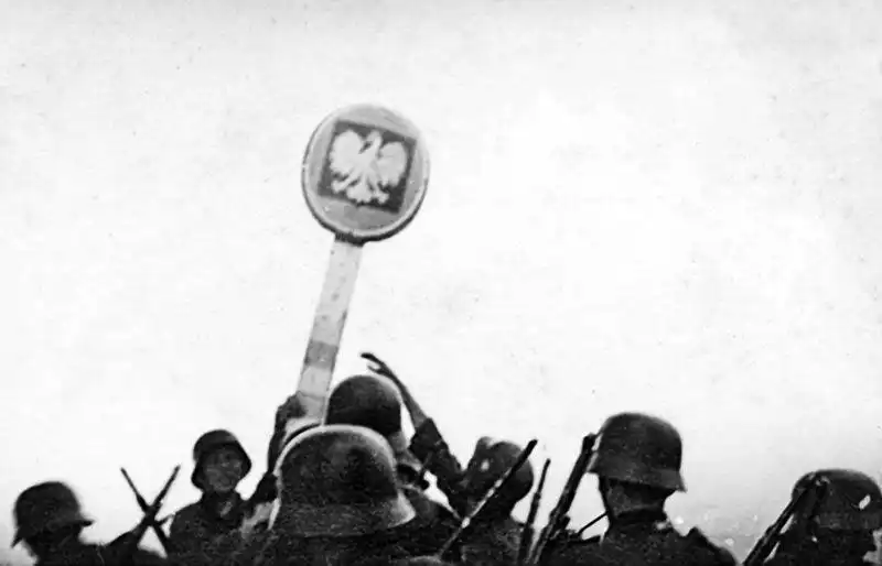 German soldiers in M35 steel helmets dismantling a round wooden Polish border post bearing the white eagle coat of arms on September 1, 1939.