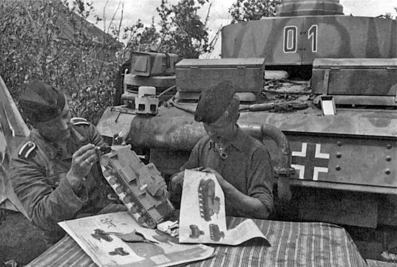 German Panzer IV tank crew assembling a paper scale model of a Soviet KV-1 heavy tank at a table on the Eastern Front in 1943.