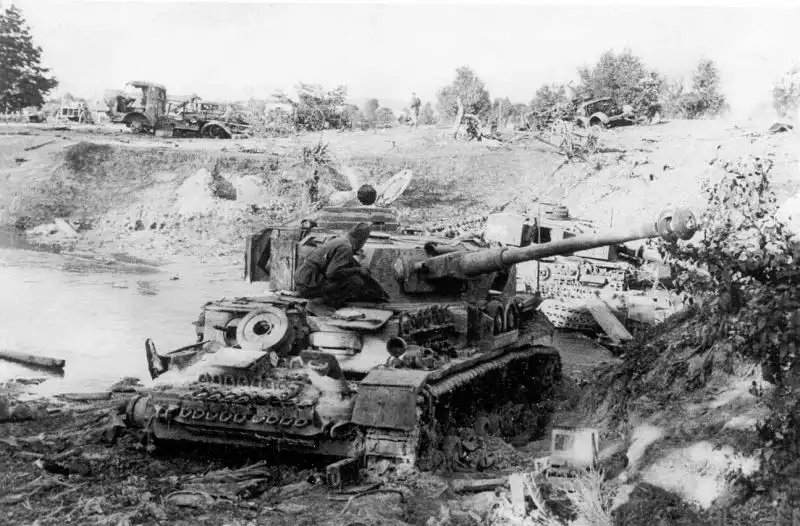 Soviet soldier inspecting a destroyed German Panzer IV tank and military convoy at a river crossing in Belarus during the summer of 1944.