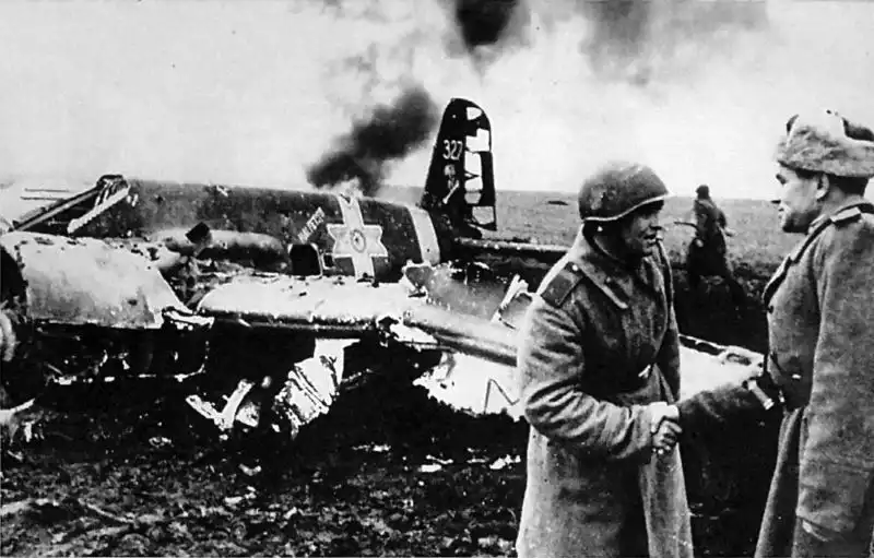 Black and white historical photo showing a Soviet officer shaking hands with an AA gun commander in front of the wreckage of a downed Romanian Henschel Hs 129B-2 aircraft, October 1943.
