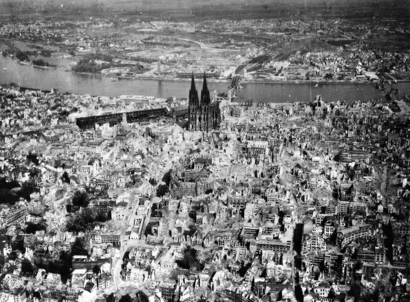 Aerial view of devastated Cologne city center with ruined buildings and standing Cologne Cathedral along the Rhine River in 1945.