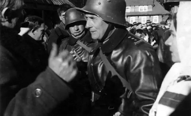 Black and white archival photo by Tadeusz Siemianowski showing Polish soldiers wearing German M35 helmets interacting with locals in Jurgów, November 1938.