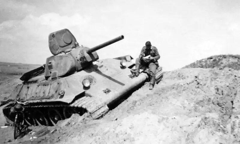 German soldier writing a letter on the armor of an abandoned Soviet T-34-76 tank in the USSR, 1941, during a brief pause in Eastern Front fighting.
