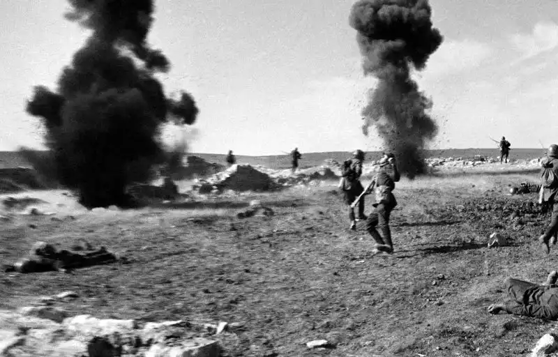 Soviet infantrymen charging forward with Mosin-Nagant bayoneted rifles under artillery smoke clouds during combat near Korpech, Crimea, photographed by Anatoly Garanin in 1942.