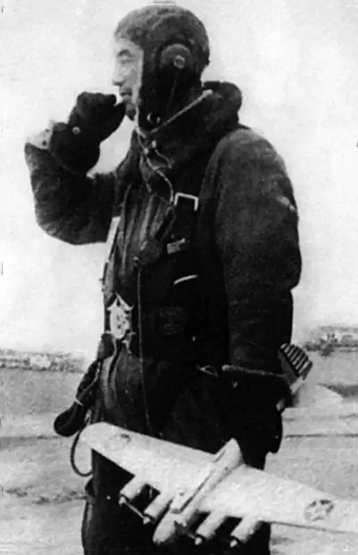 Black and white historical photo of a Japanese fighter pilot in flight gear holding a model of a four-engine B-17 Flying Fortress bomber in 1943.