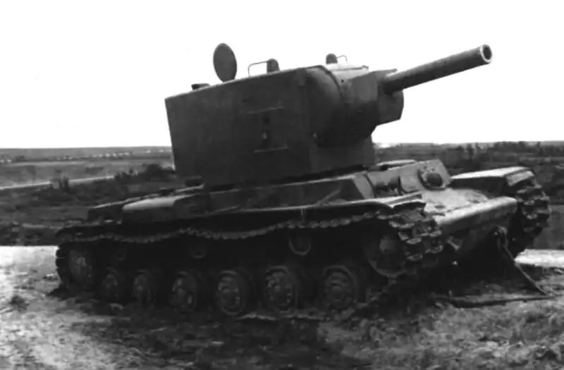 Soviet KV-2 heavy tank with a massive turret and 152mm howitzer sitting abandoned in roadside mud with attached towing cables in summer 1941.