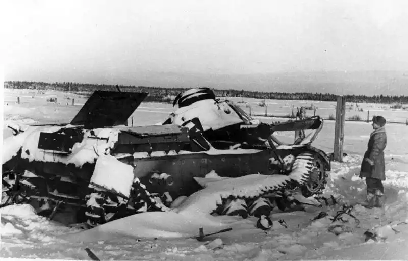 Soviet soldier in a winter coat and felt boots inspecting a destroyed German Pz.Kpfw. IV tank with internal explosion damage, Moscow region, winter 1942.