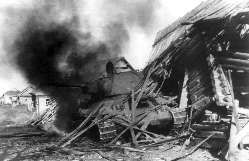 Soviet T-34/76 medium tank disabled by enemy artillery crashes through the wall of a wooden village house during combat on the Eastern Front in 1943.