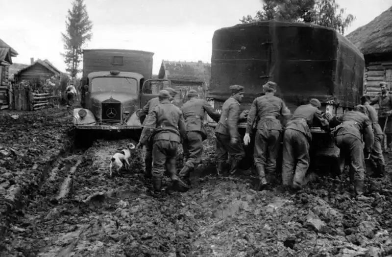 German trucks stuck in Russian mud on a Soviet road during autumn 1941, with German soldiers struggling to free their vehicles.