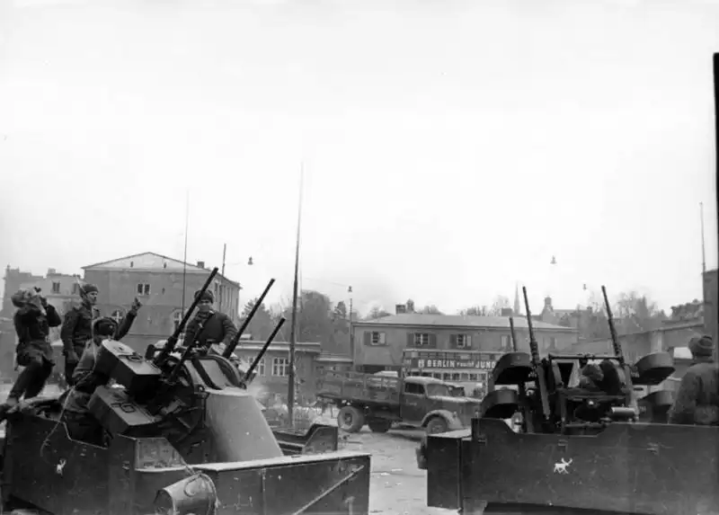 Two Soviet M17 anti-aircraft half-tracks equipped with quad 12.7mm Maxson M45 machine gun turrets stationed on a Danzig street with a captured Opel Blitz truck in the background.