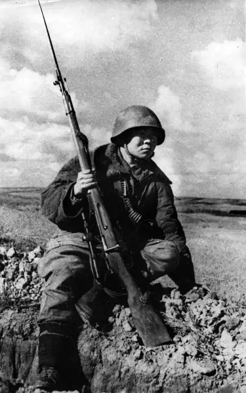 Soviet sniper Maxim Passar in padded jacket wearing SSH-40 helmet, holding a Mosin-Nagant 1891/30 rifle with PE scope and bayonet in autumn 1942.
