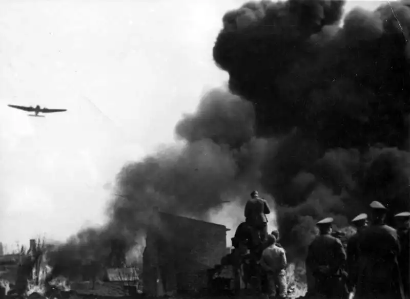 German troops advancing toward Warsaw as Heinkel He 111 bombers fly overhead above the burning city, Poland, September 1939