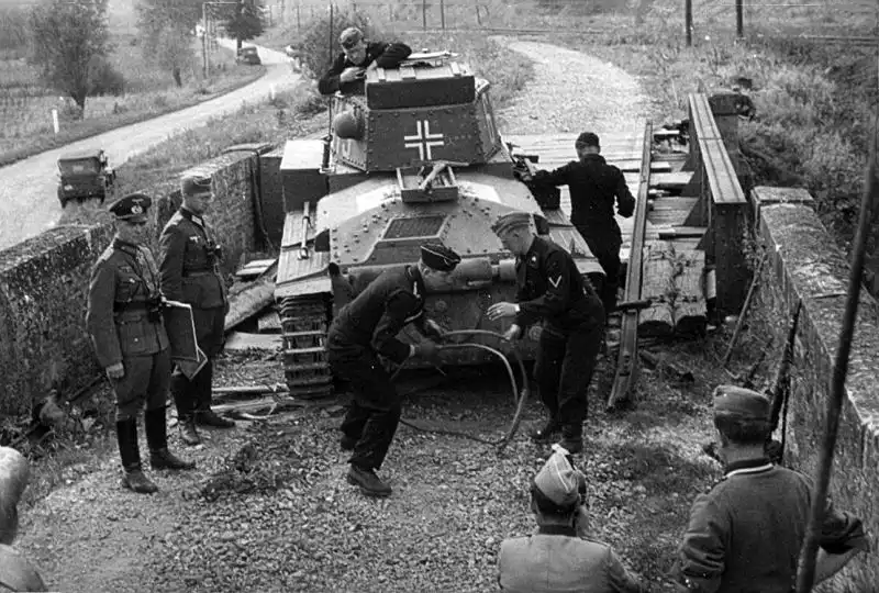 Erwin Rommel standing with map case beside a disabled Pz.Kpfw. 38(t) tank being prepared for towing in Belgium 1940.