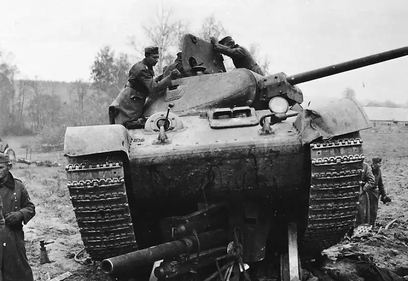 A Soviet T-34 tank sitting directly on top of a crushed German leFH 18 howitzer while Wehrmacht soldiers inspect the turret in October 1941.