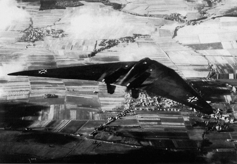 Black and white aerial photo showing an experimental Horten H.Vc flying wing aircraft in flight over fields and towns near Göttingen, 1942.