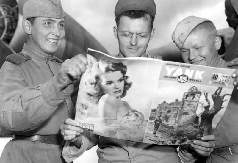 Soviet and American airmen at Poltava Air Base, Ukraine, looking at Yank magazine with Rita Hayworth on the cover, June 1944.
