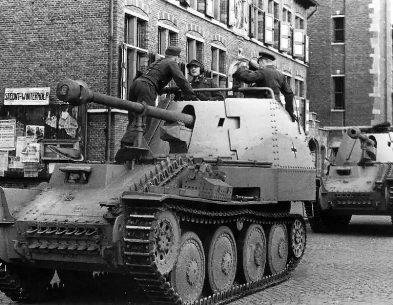 Black and white archival photo showing German Marder III Ausf. M self-propelled guns on a cobblestone market square in Eeklo, Belgium, with soldiers on board, March 1944.