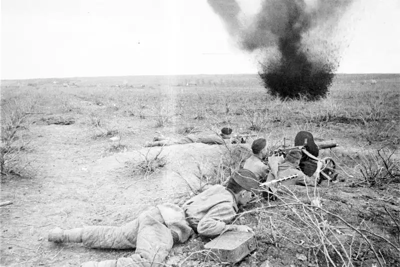 Red Army Maxim machine gun crew fighting under German artillery fire in Crimea while a Soviet soldier carries ammunition belts to the position, spring 1944
