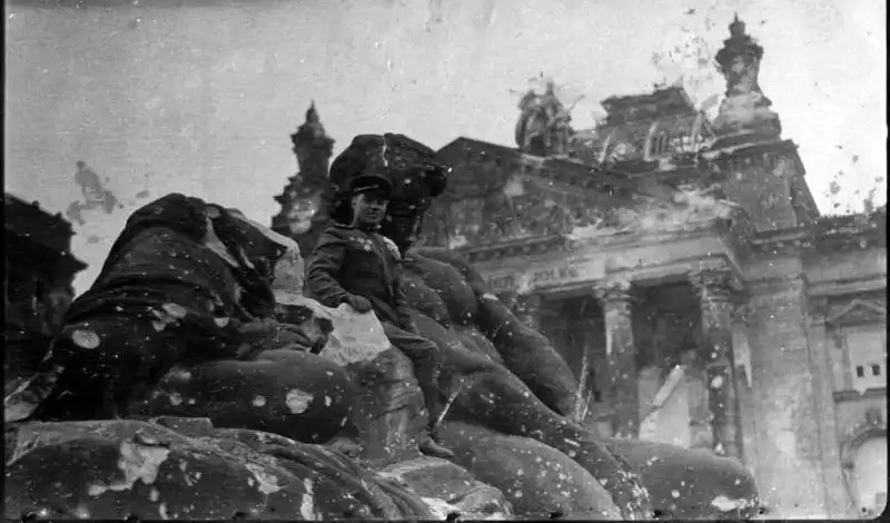 Black and white aged photograph showing Soviet tank regiment commander Colonel P. G. Mzhachikh sitting on stone ruins in front of the Reichstag in Berlin on May 9, 1945.
