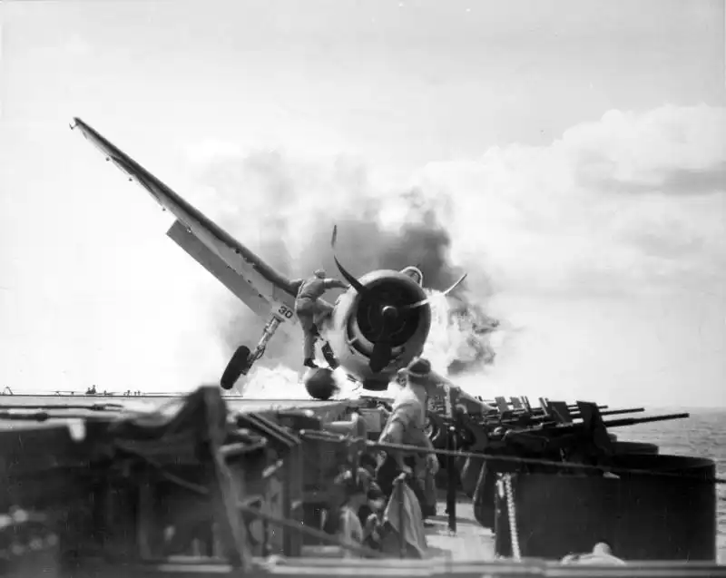 Burning F6F-3 Hellcat on USS Enterprise during emergency landing, crewman climbing onto aircraft to rescue trapped pilot, November 1943