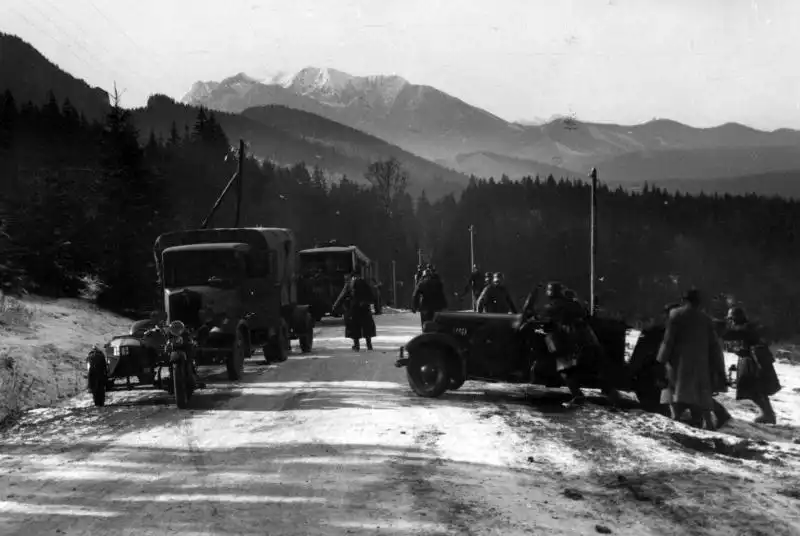Black and white historical photo showing Polish military trucks, cars, and soldiers on a snowy mountain road near Jurgów during the annexation of Czechoslovak Spiš, November 1938.