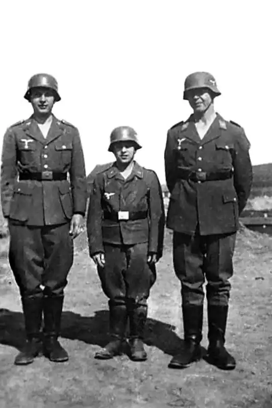 Three young German Flakhelfer auxiliaries in oversized Luftwaffe uniforms and steel helmets standing in a row in Germany, summer 1944.