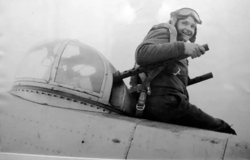 Smiling American B-25 Mitchell gunner sitting beside the twin Browning dorsal turret before a World War II combat mission.