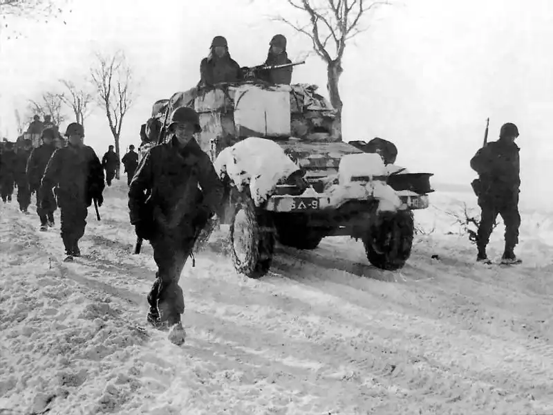 US Army infantry marching alongside a snow-covered M3 Half-Track of the 9th Armored Division in Belgium 1945.