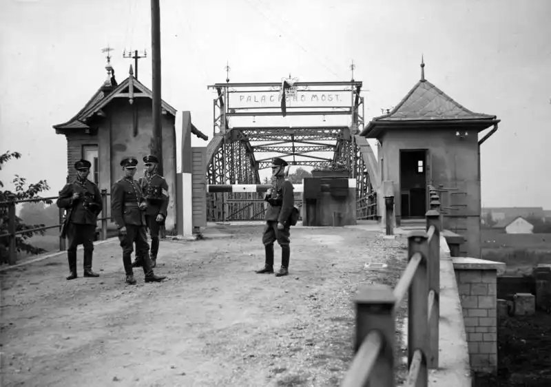 Black and white historical photo by Czesław Datka showing Polish military guards standing near a border bridge and a striped Czech border post in Bohumín, 1938.