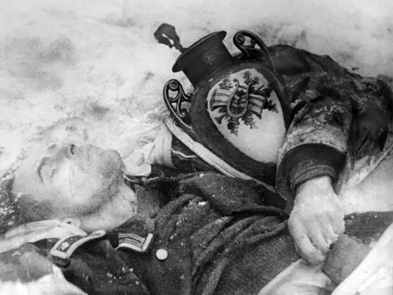Black and white archival photograph of a deceased German Oberfeldwebel lying in the snow with a decorative porcelain vase during the Battle of Moscow in 1942.