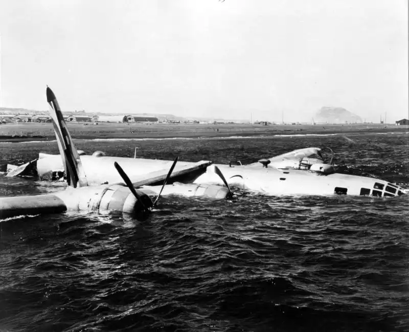 Crashed American B-29 Superfortress missing its tail section lies in shallow water near Iwo Jima after returning from a bombing mission against Japan, with Mount Suribachi visible in the background.