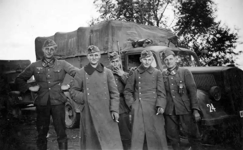Group of Wehrmacht soldiers in coats and tunics posing near an Opel Blitz 3-ton military truck in Poland September 1939.