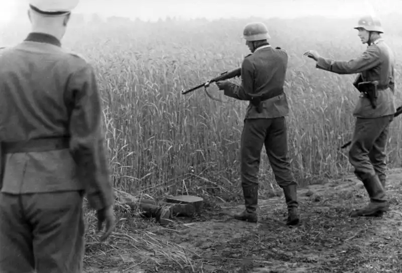 German field gendarmerie soldiers standing over a fallen wounded Soviet sniper near a grain field in Vitebsk, July 1941.