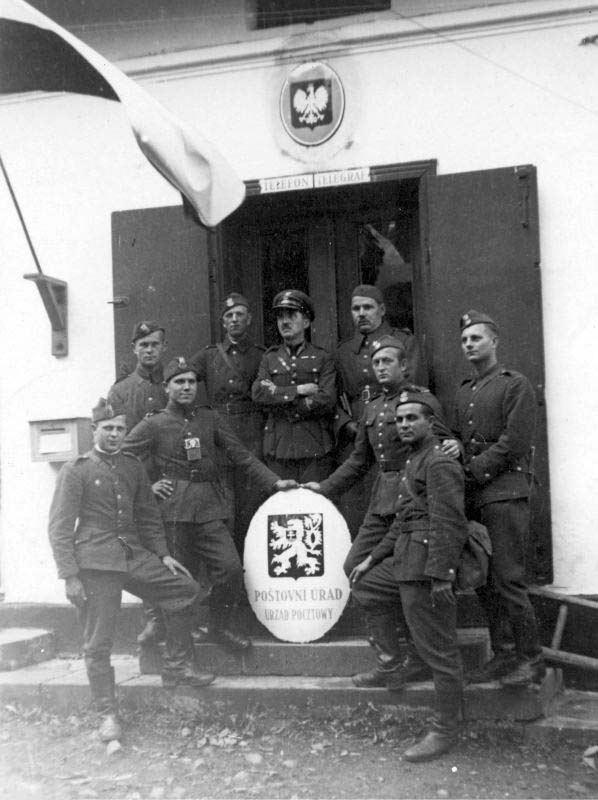 Black and white historical photo from NAC showing Polish soldiers and policemen posing on steps with a low-slung Czechoslovak emblem in front of a post office building in 1938.