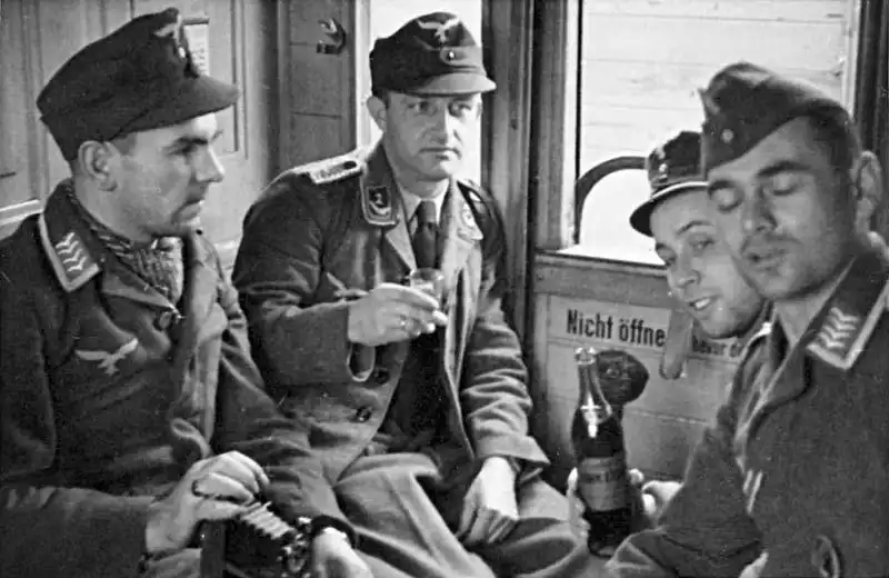 Luftwaffe personnel drinking and holding a folding camera inside a train compartment in occupied France during WWII.