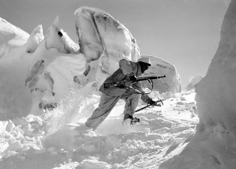 German Gebirgsjäger soldier in white snow camouflage traversing a steep snow slope surrounded by ice icebergs with an ice axe and rifle in 1942.