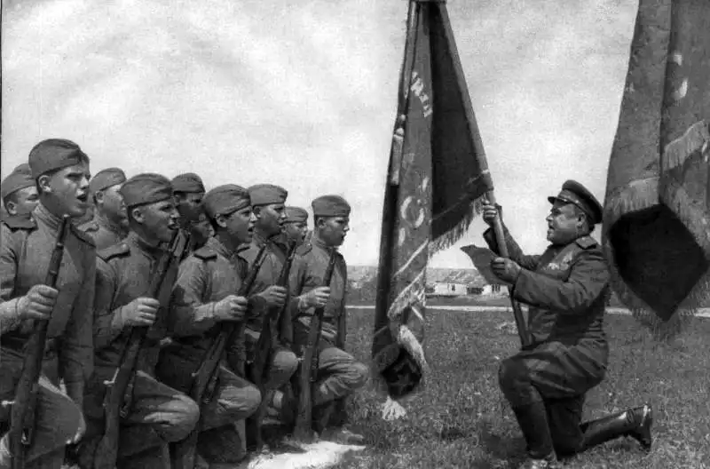 Young Soviet Red Army recruits kneeling before a battle flag while taking the military oath during a ceremony in the USSR, summer 1944.