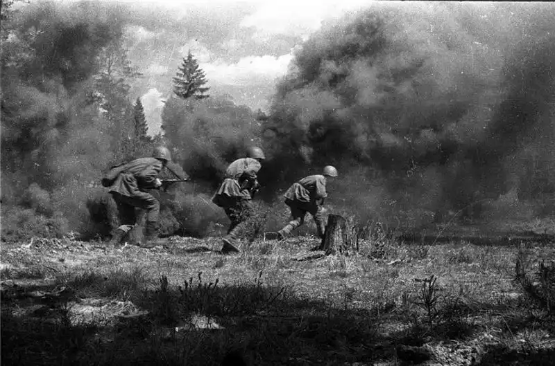 Black and white action photo by Mikhail Savin showing Soviet soldiers running through dense smoke during a combat operation in 1943.