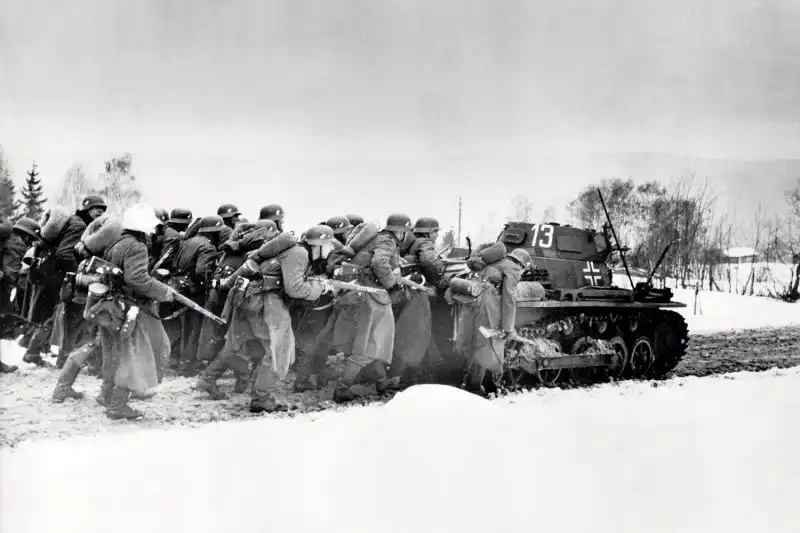 German infantrymen armed with Mauser rifles take cover behind a Panzer I light tank while advancing along a mountain road during the invasion of Norway in 1940.