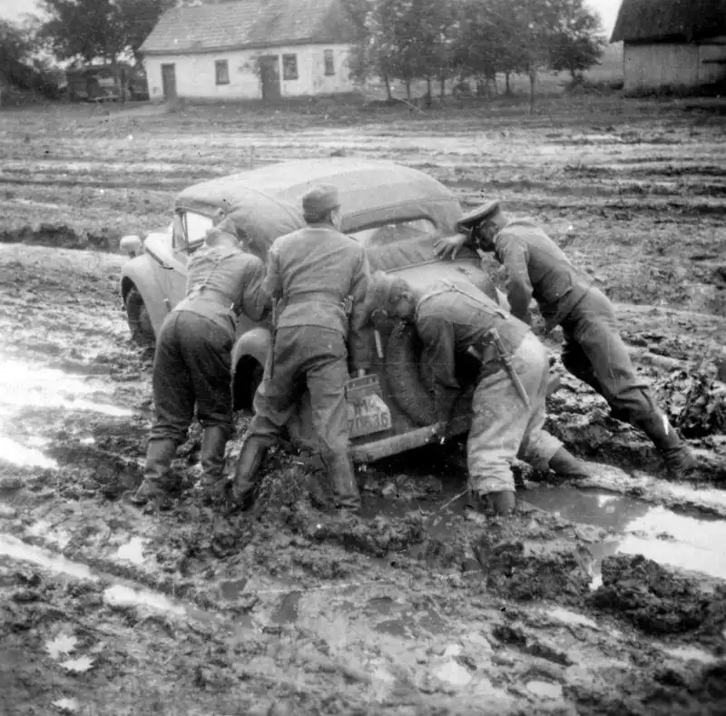 German soldiers and an officer pushing a stuck Opel passenger car with Lower Saxony plates out of deep Russian mud in an occupied Soviet village, 1941