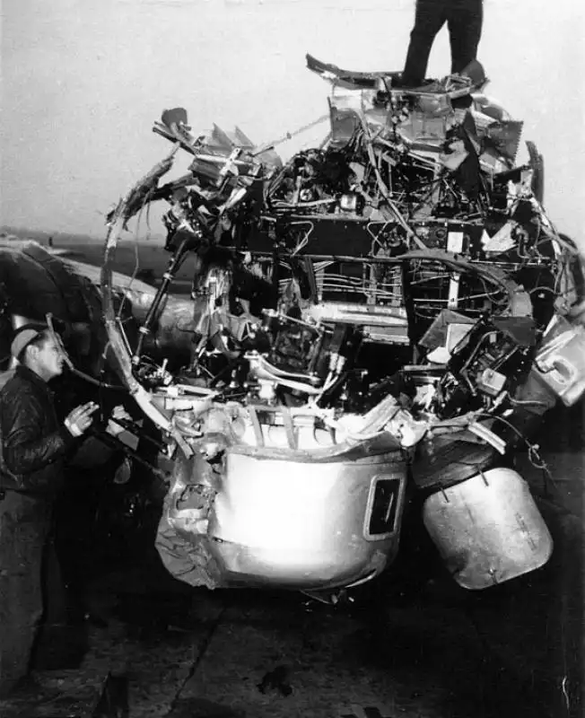 US Army Air Force mechanic examining the exposed, shattered nose structure of damaged B-17G Flying Fortress in England.
