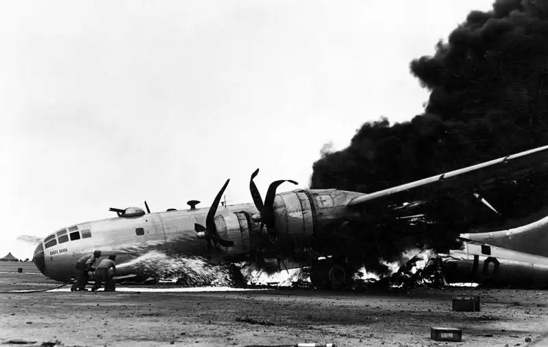 Battle-damaged B-29 Superfortress burning after a crash landing on Iwo Jima in 1945, with mission markings visible on the fuselage.