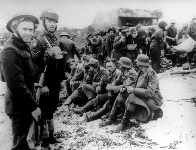 Canadian troops and Military Police guarding captured German prisoners from the 716th Static Infantry Division on Juno Beach 1944.
