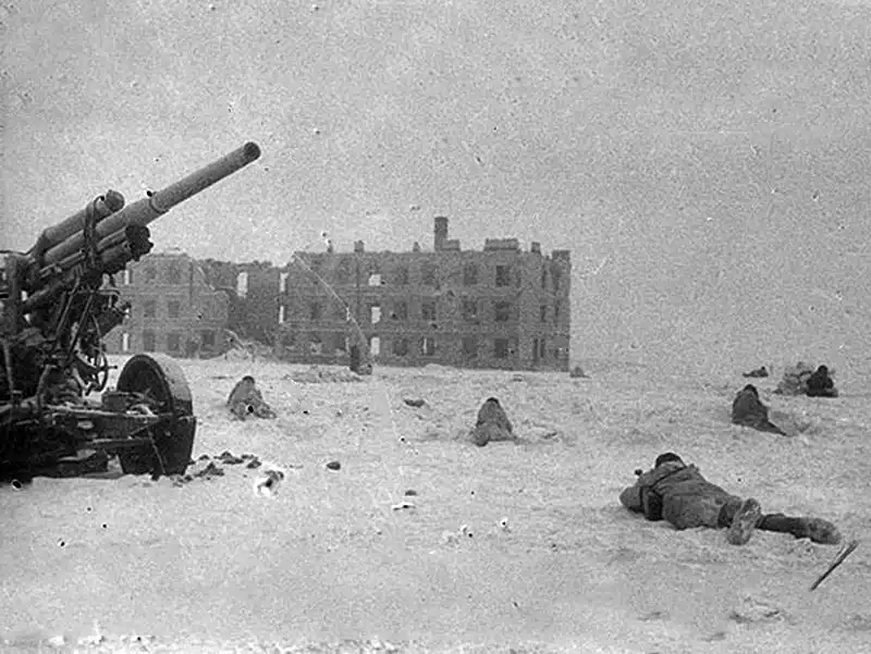 Soviet infantry wearing white camouflage suits lying in snow near a damaged 76.2mm anti-aircraft gun during winter combat in Stalingrad 1942.