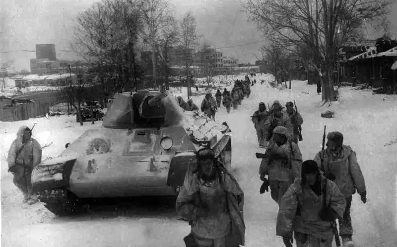 Soviet soldiers in white camouflage and a winter-camouflaged T-34 tank marching through liberated Klin during the Battle of Moscow, December 1941.