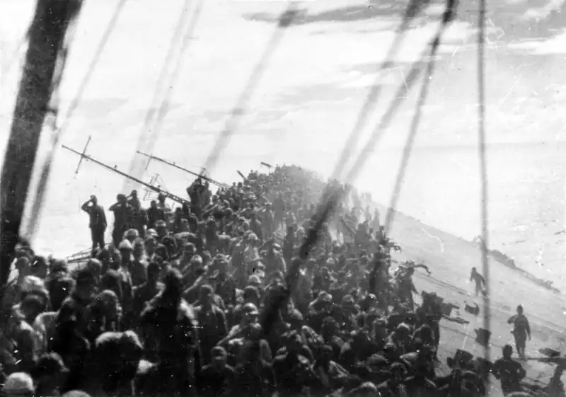 Japanese sailors gathered on the stern of the sinking aircraft carrier Zuikaku during the final lowering of the naval flag at the Battle of Leyte Gulf, October 1944.