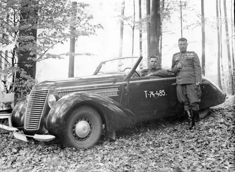 Black and white historical photo showing a Soviet Red Army colonel standing next to a sleek, dark Steyr 220 Gläser Roadster sports car with a driver inside, May 1945.