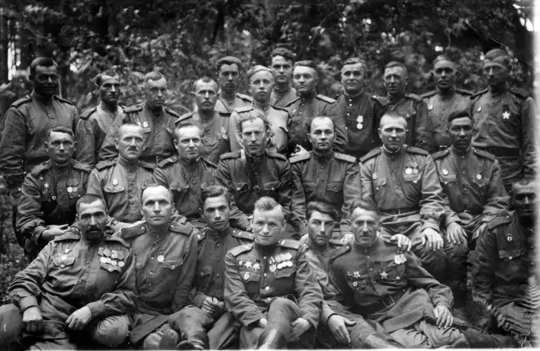 Black and white historical group photograph showing Soviet Red Army soldiers and officers in uniform posing in a forest in May 1945.