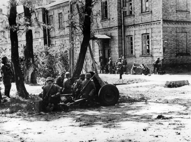 Black and white archival photo from RGAKFD showing German soldiers with a 37mm PaK anti-tank gun near a brick building in the Eastern Fort of Brest Fortress in 1941.